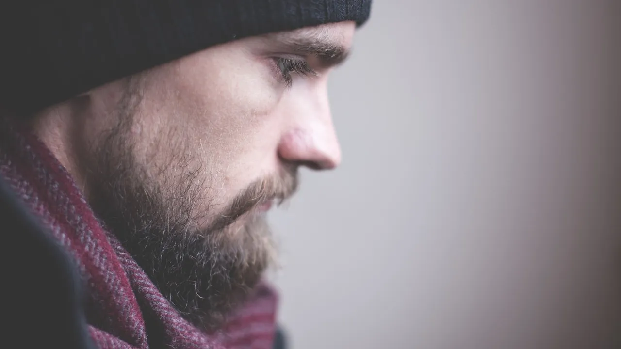 Un homme de profil, le regard baissé, sur un fond clair